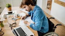 Young business owner in wheelchair working on papers at table with laptop